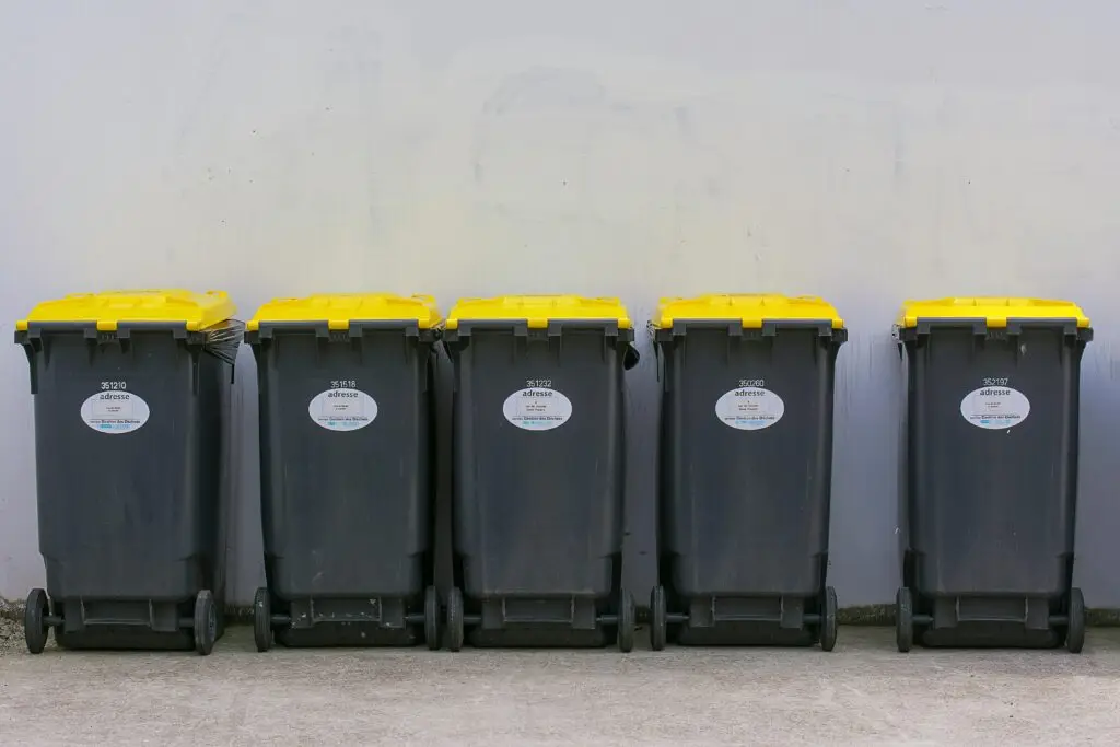 Neatly lined up garbage bins with yellow lids against a plain background wall.